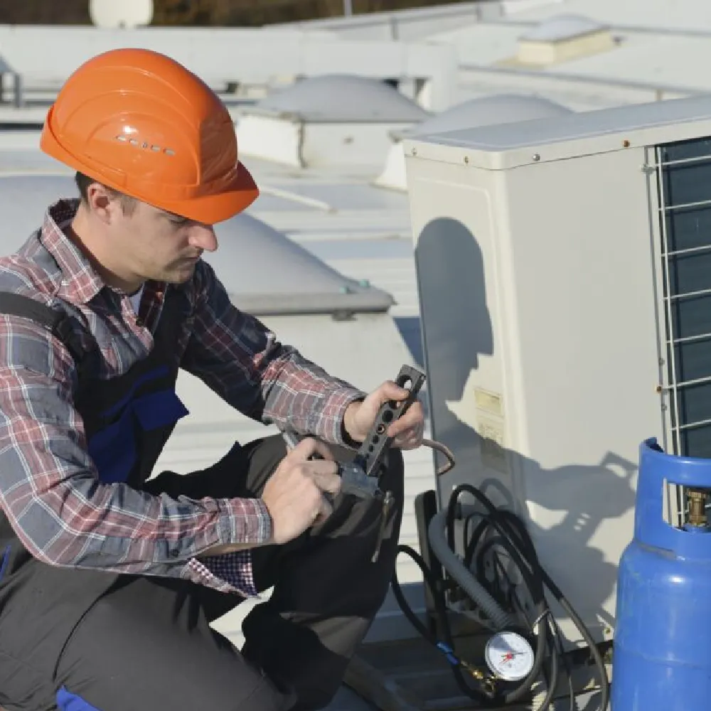 Rooftop HVAC technician connecting refrigerant cylinder and gauges to an outdoor condenser unit.