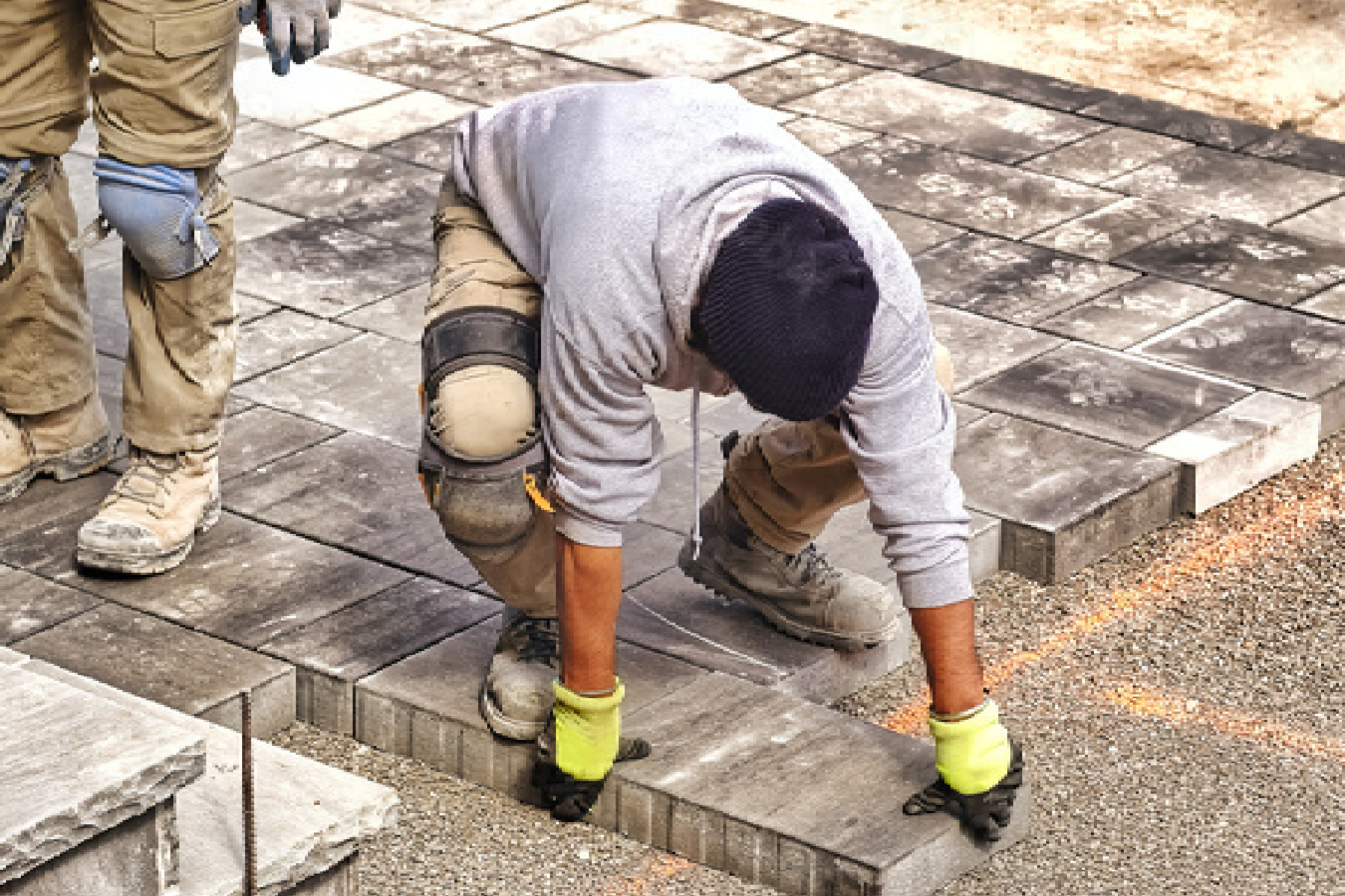 Landscaper positioning concrete pavers on a driveway or patio in Adelaide.