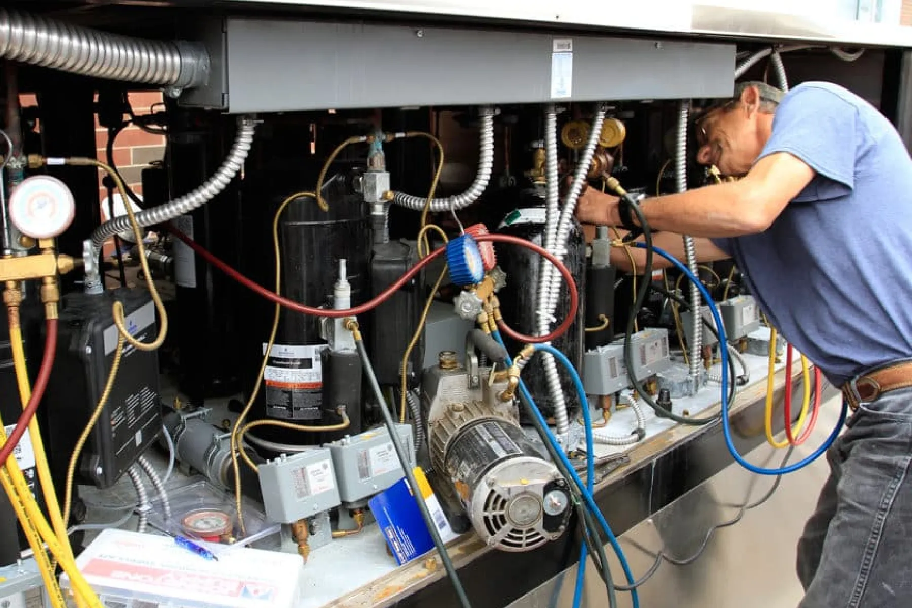 HVAC technician servicing commercial air conditioning compressors with manifold gauges and electrical components.