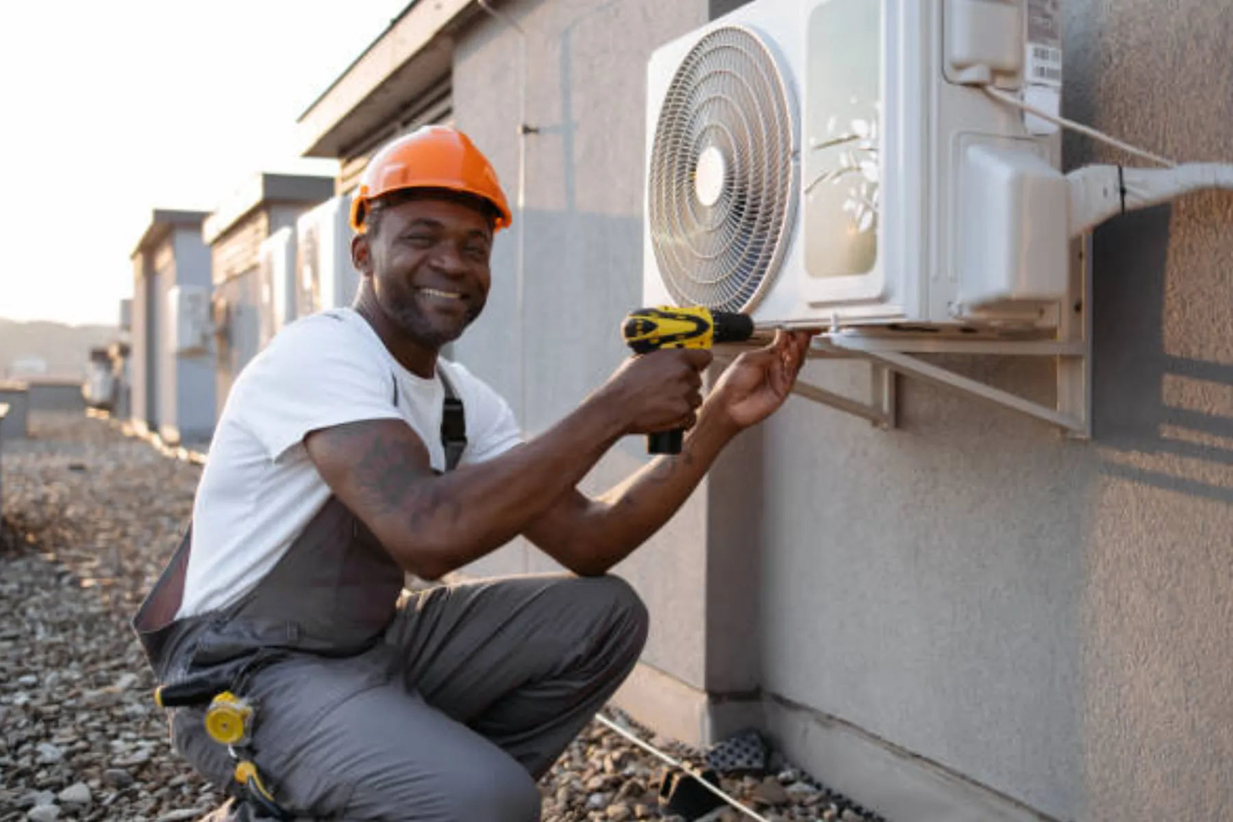 Technician securing a wall-mounted air conditioning condenser with a cordless drill.