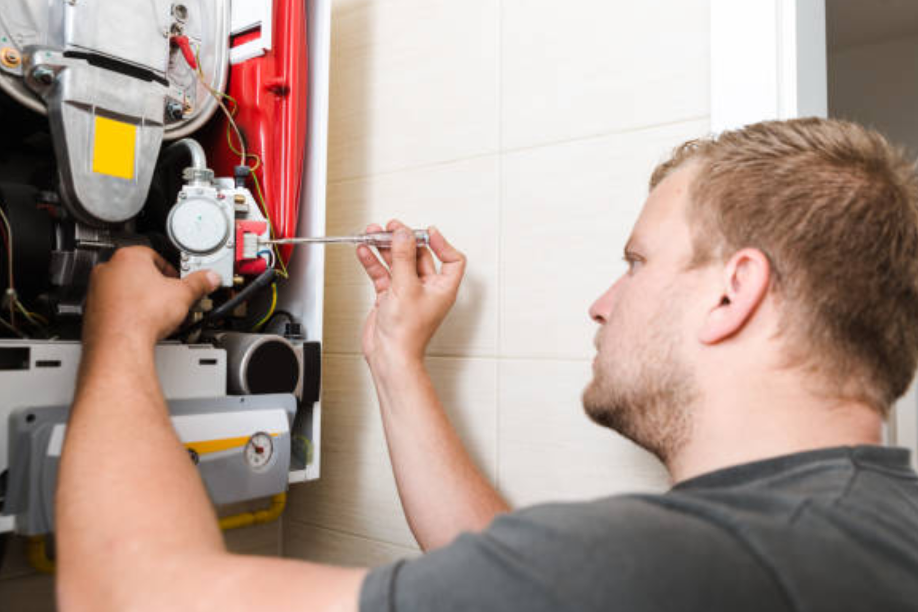 Plumber adjusting components inside a gas hot water unit with a wrench.