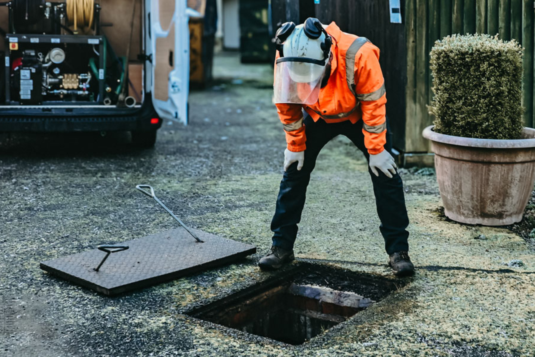Plumber in hi‑vis gear inspecting an open manhole for drainage maintenance.